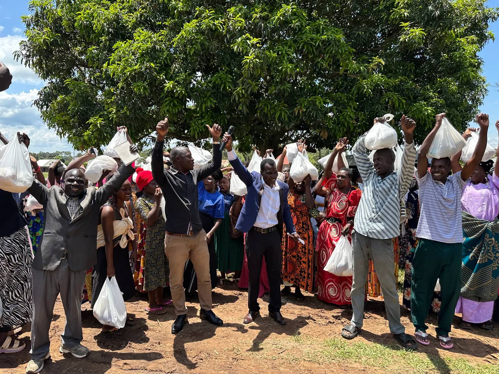 Community members gather beneath a tree with food packages.
