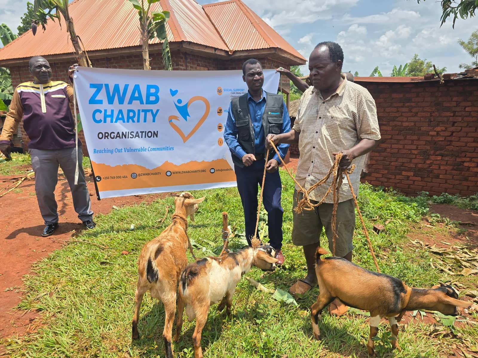 Community members stand with goats beside a Zwab project banner.