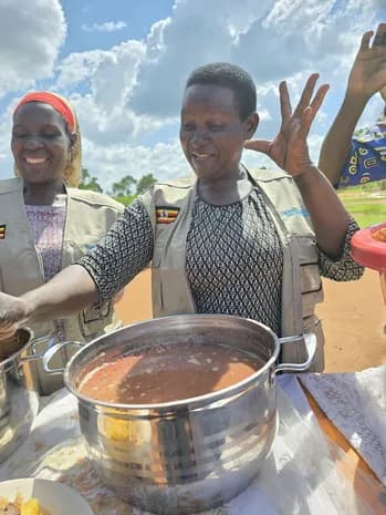 Team members stand beside a pot of food.