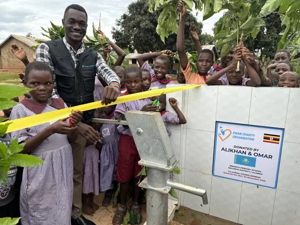 A child and an adult hold a ribbon beside a handpump.