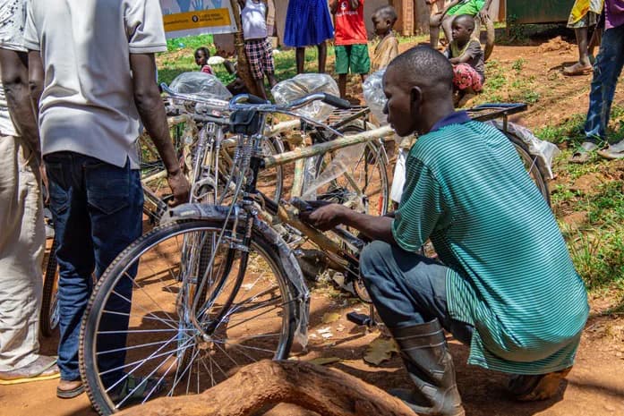 A man crouches beside a bicycle among a group of bicycles.