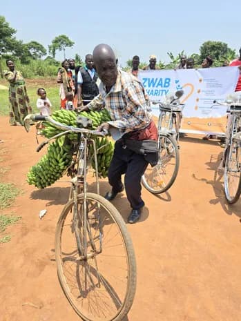 A man straddles a bicycle carrying green bananas.