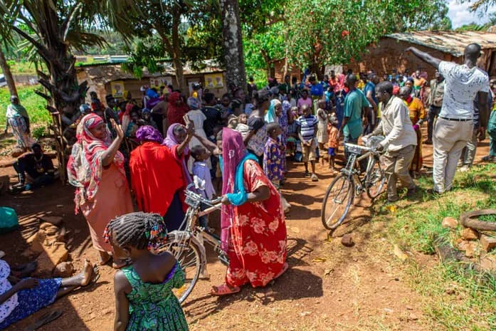 People gather with bicycles near buildings and trees.