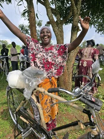 A woman raises her hands beside a bicycle.