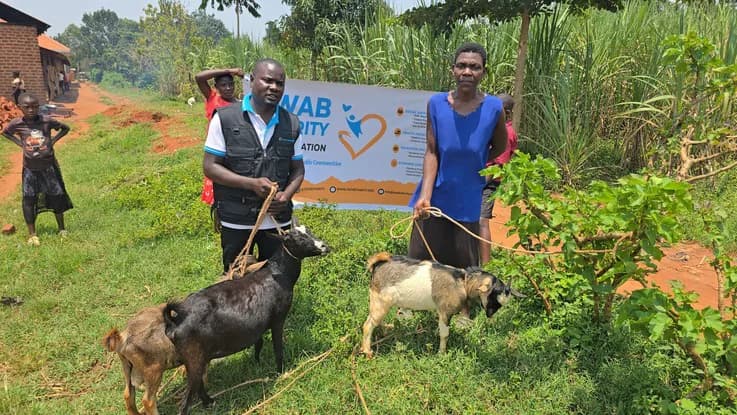 Two people stand with goats beside a Zwab banner.