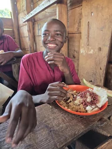 A child holds a plate of food at a table.