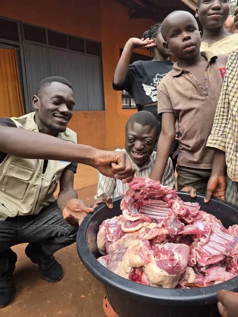 Adults and children gather beside a basin of meat.