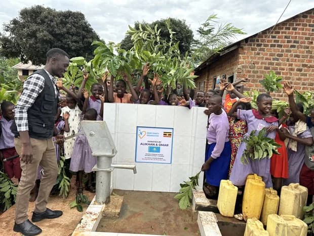 Children and an adult gather beside a handpump.